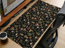 Black desk mat with a dark academia botanical pattern featuring mushrooms, insects, and forest foliage.