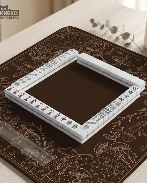 Dark brown mahjong table mat with a botanical border of moths, mushrooms, keys, vines, and small celestial details around a plain open center.