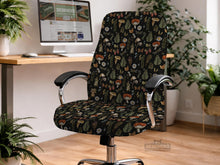A black chair cover with a botanical print of mushrooms, ferns, daisies, berries, snails, and butterflies on a chair.