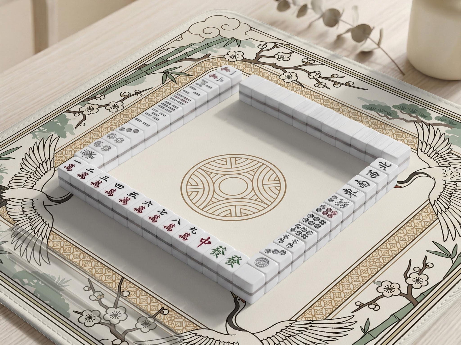 Square mahjong table mat with a cream center and a border design of cranes, bamboo, plum blossoms, and a geometric frame in sage green and warm gold.
