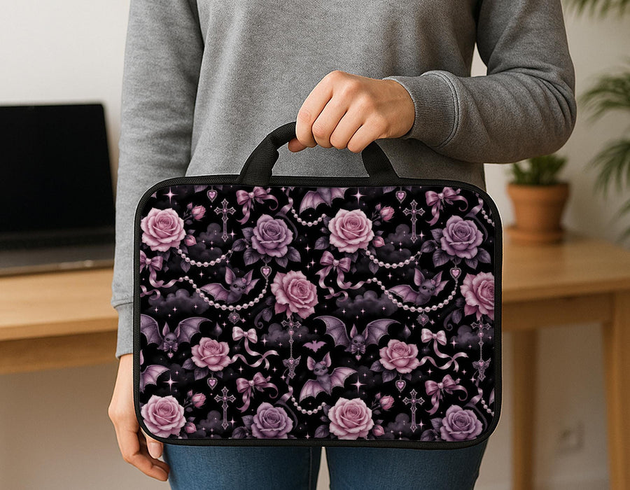 Pink laptop sleeve case with pastel goth print showing roses, small bats, bows, pearl chains, smoky clouds, and sparkle details.