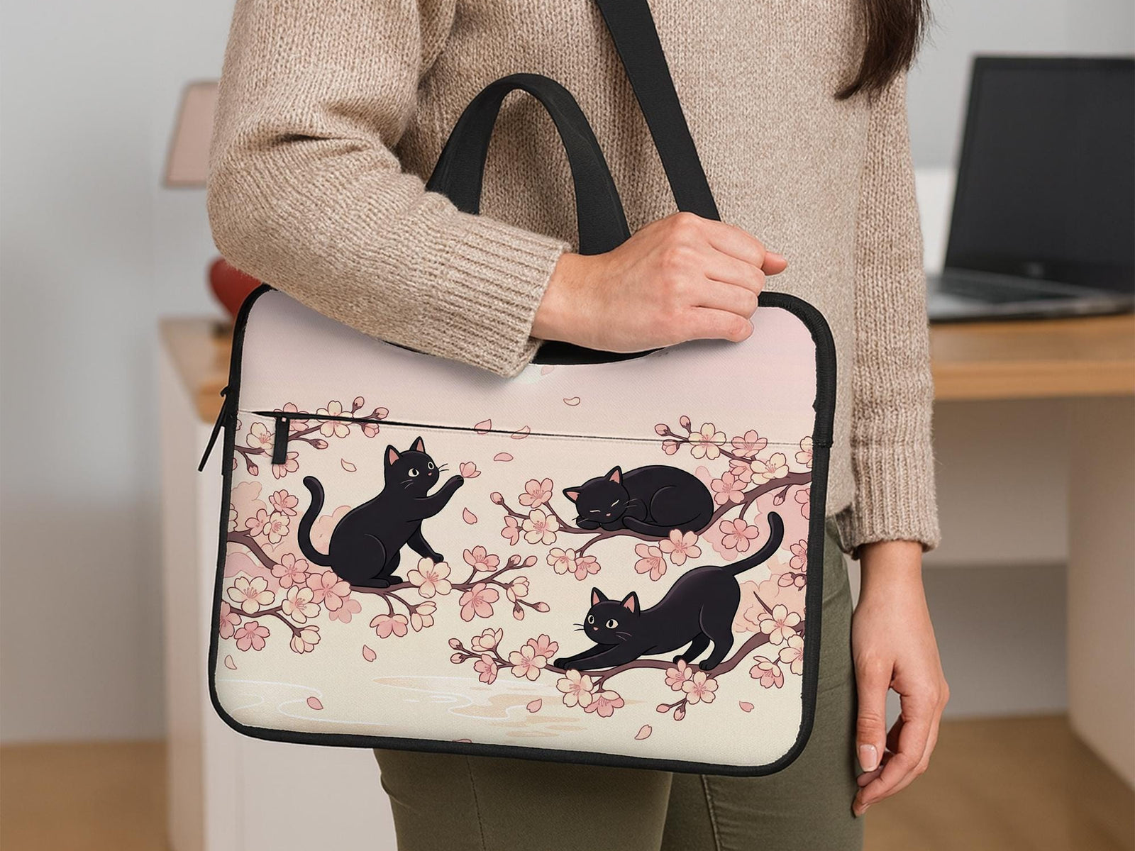 Pink laptop sleeve case with black cat illustrations, sakura flowers, and falling petals in a repeating Japanese-inspired pattern.