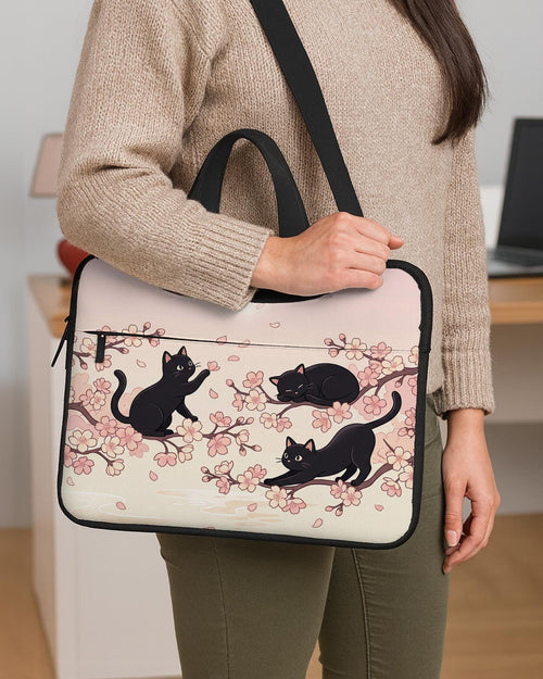 Pink laptop sleeve case with black cat illustrations, sakura flowers, and falling petals in a repeating Japanese-inspired pattern.