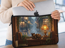 Laptop sleeve with a dark academia illustration showing a curled-up cat, rain-streaked window, glowing lamp, wooden shelves, stacked books, and ivy details.