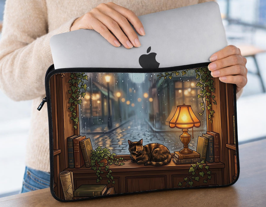Laptop sleeve with a dark academia illustration showing a curled-up cat, rain-streaked window, glowing lamp, wooden shelves, stacked books, and ivy details.