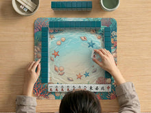 Square mahjong mat with coastal seashell artwork featuring coral, starfish, scallops, and aqua water colors around a lighter center area.