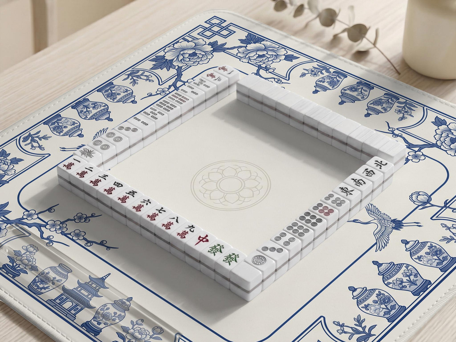 Blue and white mahjong mat with floral peonies, blossom branches, and porcelain jar illustrations around a clean center.