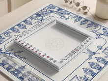 Blue and white mahjong mat with floral peonies, blossom branches, and porcelain jar illustrations around a clean center.
