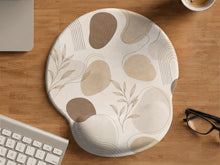 Beige ergonomic mouse pad with a neutral abstract botanical pattern and a raised wrist support area on one side.