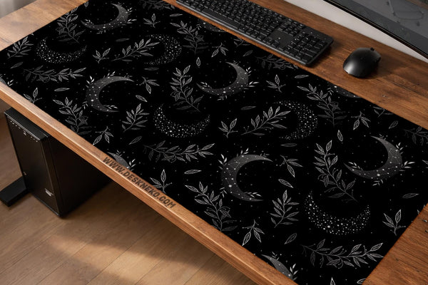 A black desk mat with a crescent moon, scattered stars, and leafy botanical branches in a celestial pattern.