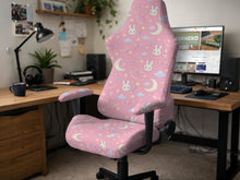 Pink chair cover with bunny faces, crescent moons, clouds, and bows on a white chair.