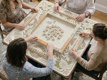 Square mahjong mat with a light floral border in sage green, cream, and blush around a plain center play area.