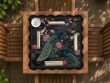 Square black mahjong mat with a gold peacock, blush flowers, and dark botanical artwork on a dark background.