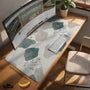 A desk mat with sage green abstract blocks, cream space, gray stone-like shapes, fine topographic contour lines, and small branch details.