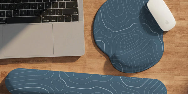Muted blue desk mat with thin topographic line art pattern shown with matching mousepad and keyboard wrist rest options.