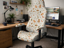 A gaming chair cover with a woodland animal print featuring foxes, rabbits, bears, mushrooms, and leaves in green, brown, and beige tones.