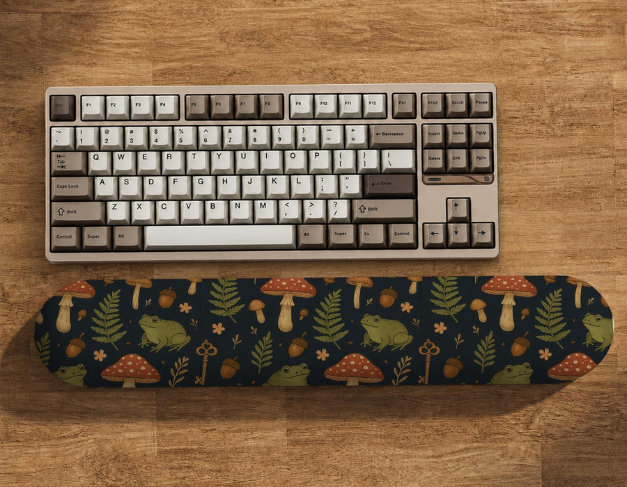 Dark botanical desk mat options with frogs, mushrooms, ferns, and acorns in brown and green tones, plus a matching keyboard wrist rest.