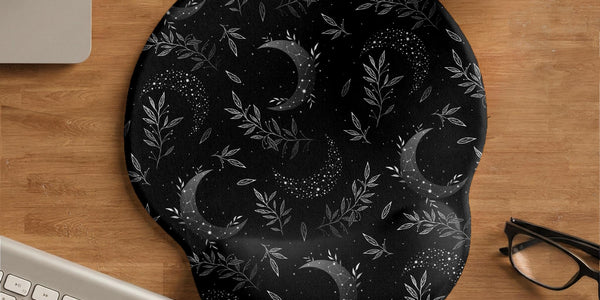 Black mouse pad and wrist rest with moon phases, small stars, and fine botanical accents in a dark floral pattern.