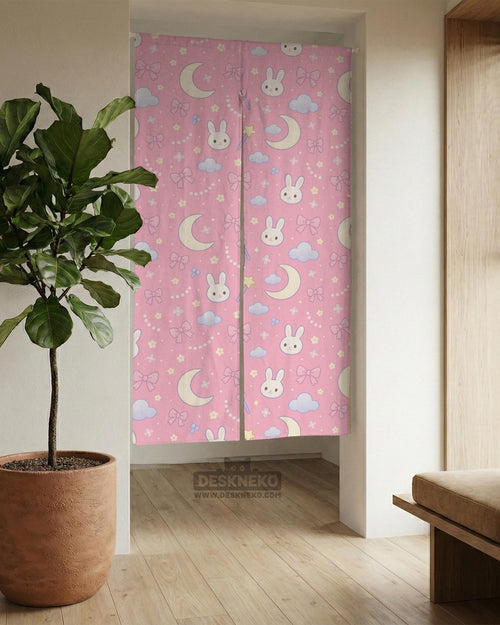 Pink noren curtain with cute bunny faces, crescent moons, blue clouds, bows, stars, and small flowers on a warm pink background.