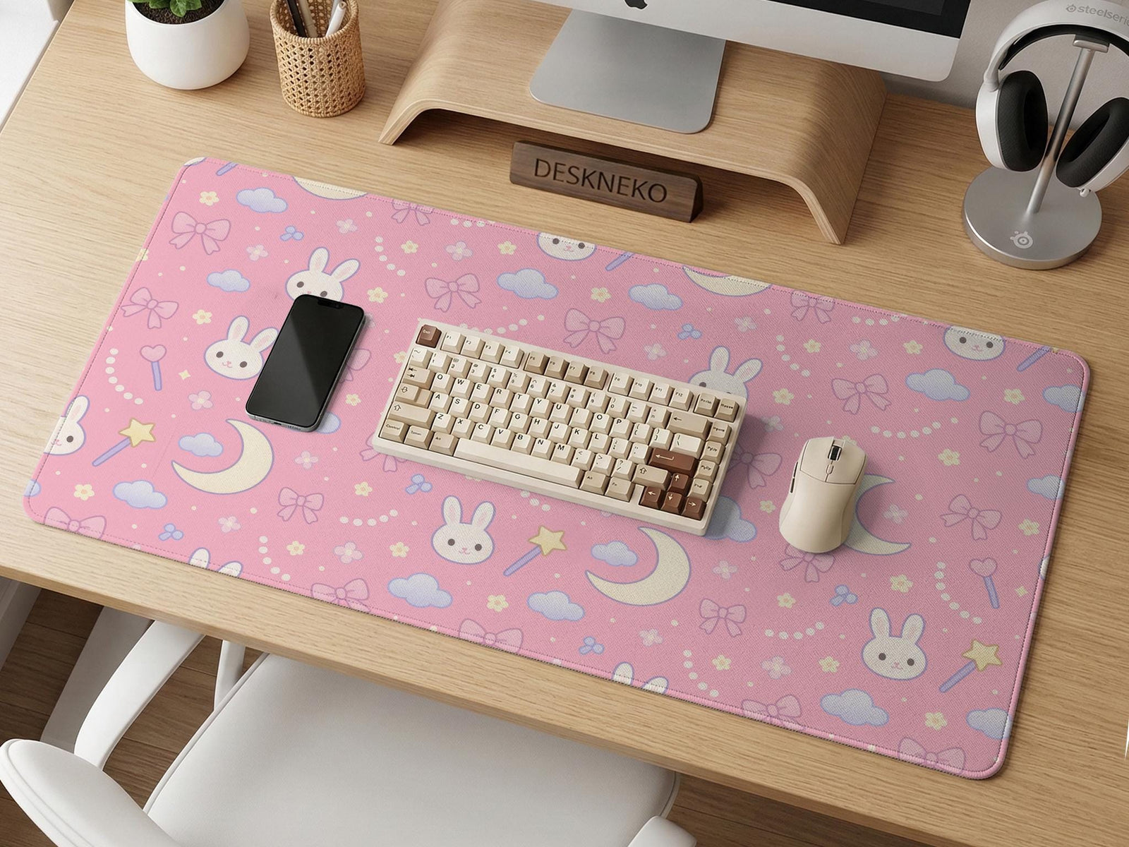 Pink desk mat with a kawaii design featuring bunnies, clouds, moons, bows, flowers, and a small magic wand pattern.