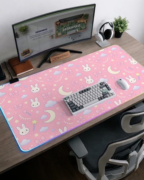 Pink desk mat with pastel bunnies, moons, clouds, bows, and stars on a light background.