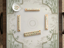 A square cream mahjong mat with sage bamboo corners and soft cloud details around an open center area.