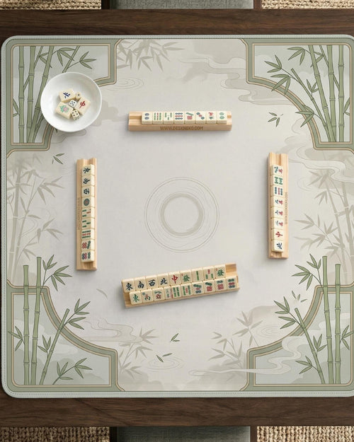 A square cream mahjong mat with sage bamboo corners and soft cloud details around an open center area.