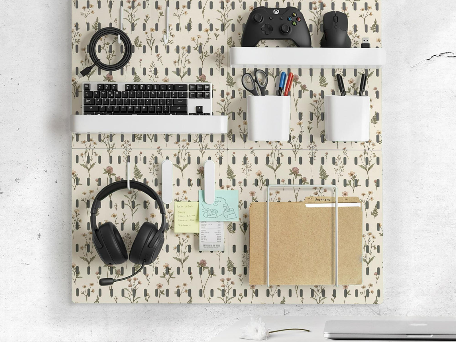 Cream pegboard wall organizer with small floral print, sage green stems, black slot layout, shelves, hooks, clips, and containers.