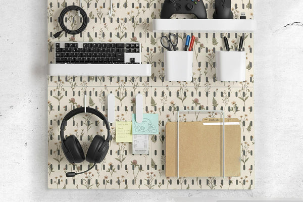 Cream pegboard wall organizer with small floral print, sage green stems, black slot layout, shelves, hooks, clips, and containers.