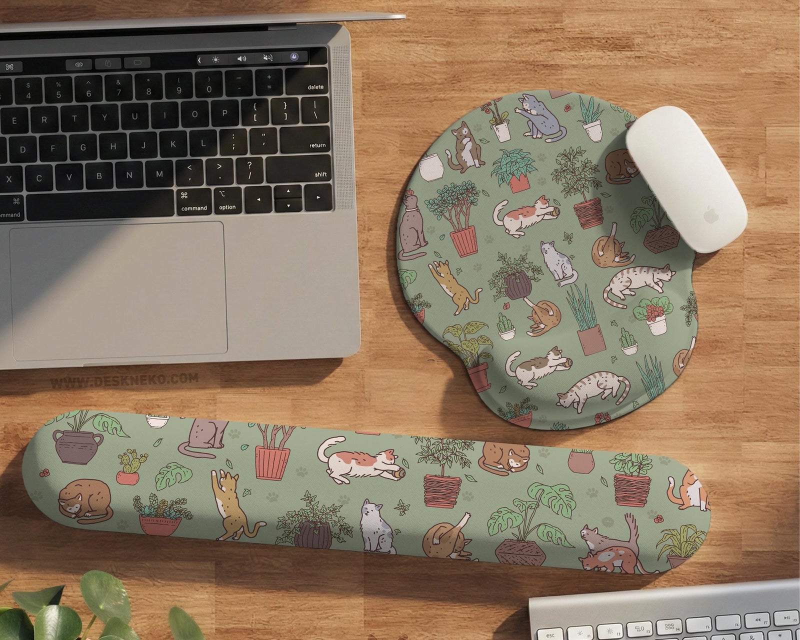Sage green desk mat with a pattern of lounging cats, leafy plants, cactus pots, and earthy botanical details.