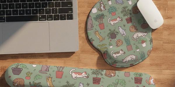 Sage green desk mat with a pattern of lounging cats, leafy plants, cactus pots, and earthy botanical details.