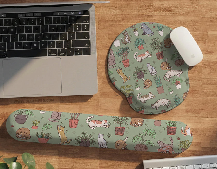 Sage green desk mat with a pattern of lounging cats, leafy plants, cactus pots, and earthy botanical details.