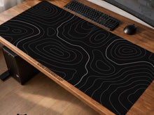 Black desk mat with a thin gray topographic contour line pattern.