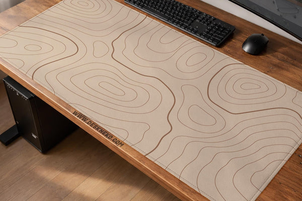 Beige desk mat with thin topographic contour lines in a minimal pattern.