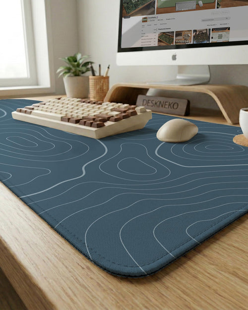 A slate blue desk mat with thin contour line map art on a light background.