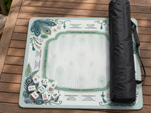 Teal square mahjong mat with peacock feathers, soft floral pattern, tassel details, and printed rule guide text in the center.