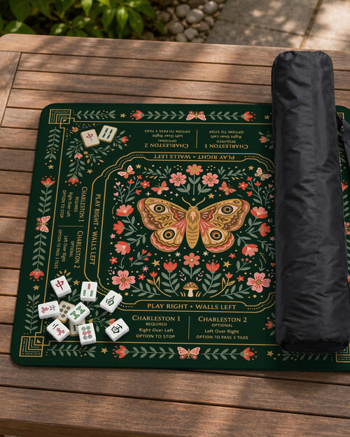Dark botanical mahjong table mat with a floral border, large moth and butterfly design in the center, gold corner frame, and printed rules layout around the edge.