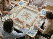 A square mahjong mat with blue hydrangea flowers, green vines, a cream background, a striped center, and printed rules around the border.