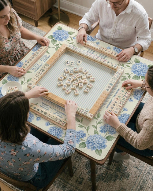 A square mahjong mat with blue hydrangea flowers, green vines, a cream background, a striped center, and printed rules around the border.