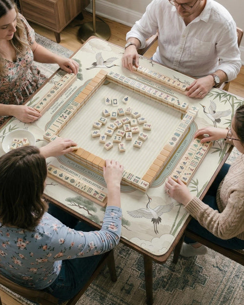 Sage green square mahjong mat with a chinoiserie design featuring cranes, bamboo, blossoms, and mountains, with rules printed around the border.