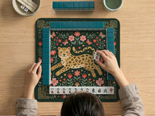 Green square mahjong mat with a leopard in folk art style, surrounded by flowers, butterflies, stars, and mushrooms with a gold border.