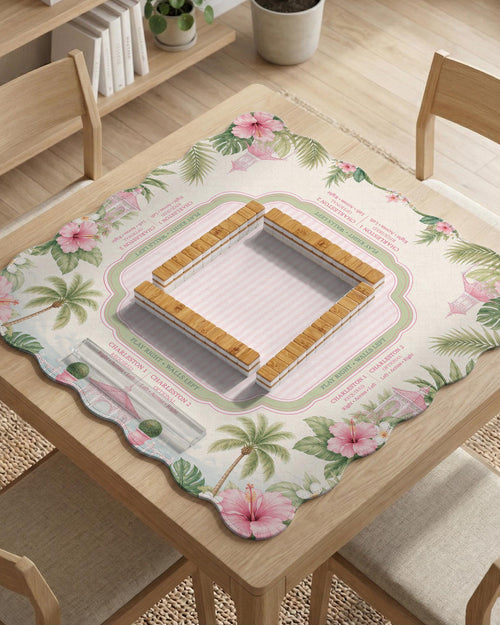 Pink mahjong mat with a scalloped edge design, palm leaves, hibiscus flowers, soft sage accents, and a striped center play area with printed rules around the border.