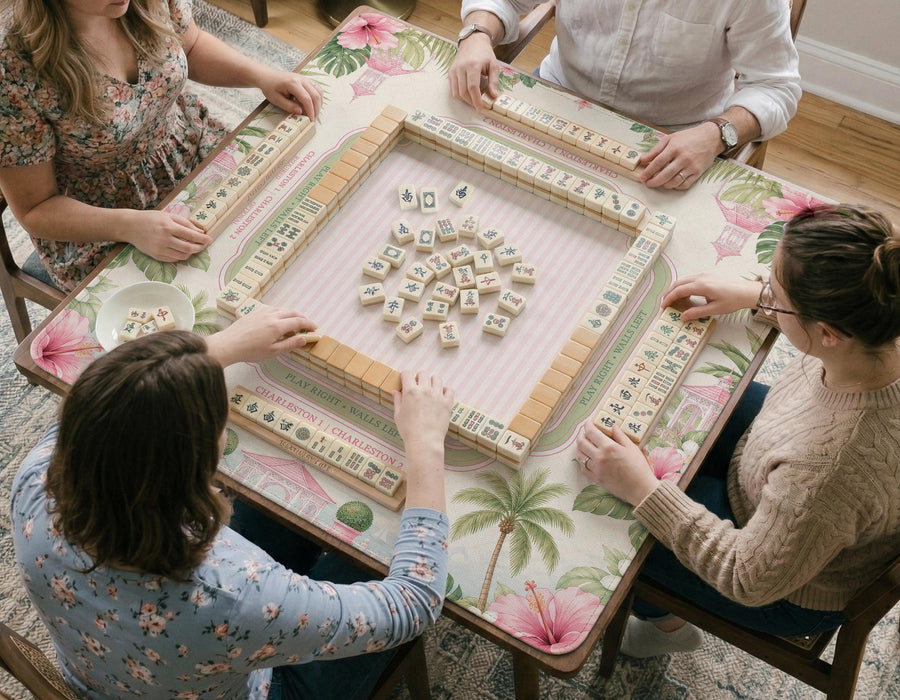 Pink mahjong mat with hibiscus flowers, palm leaves, sage green borders, a cream textured background, and a striped center area for tile play.