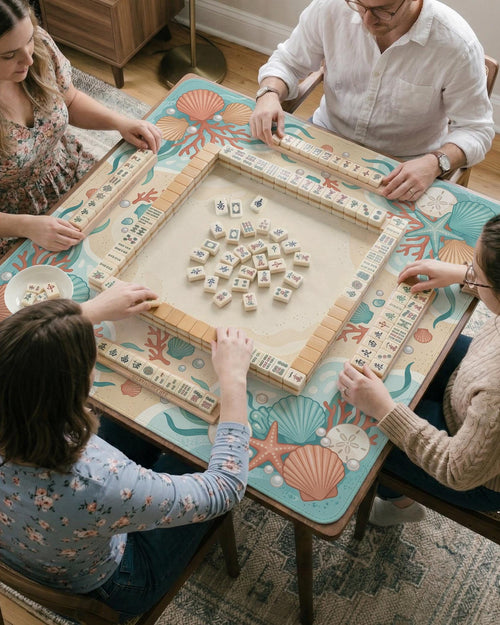 Square mahjong mat with a coral and aqua coastal border featuring shells, coral, pearls, starfish, and waves around a clear center.