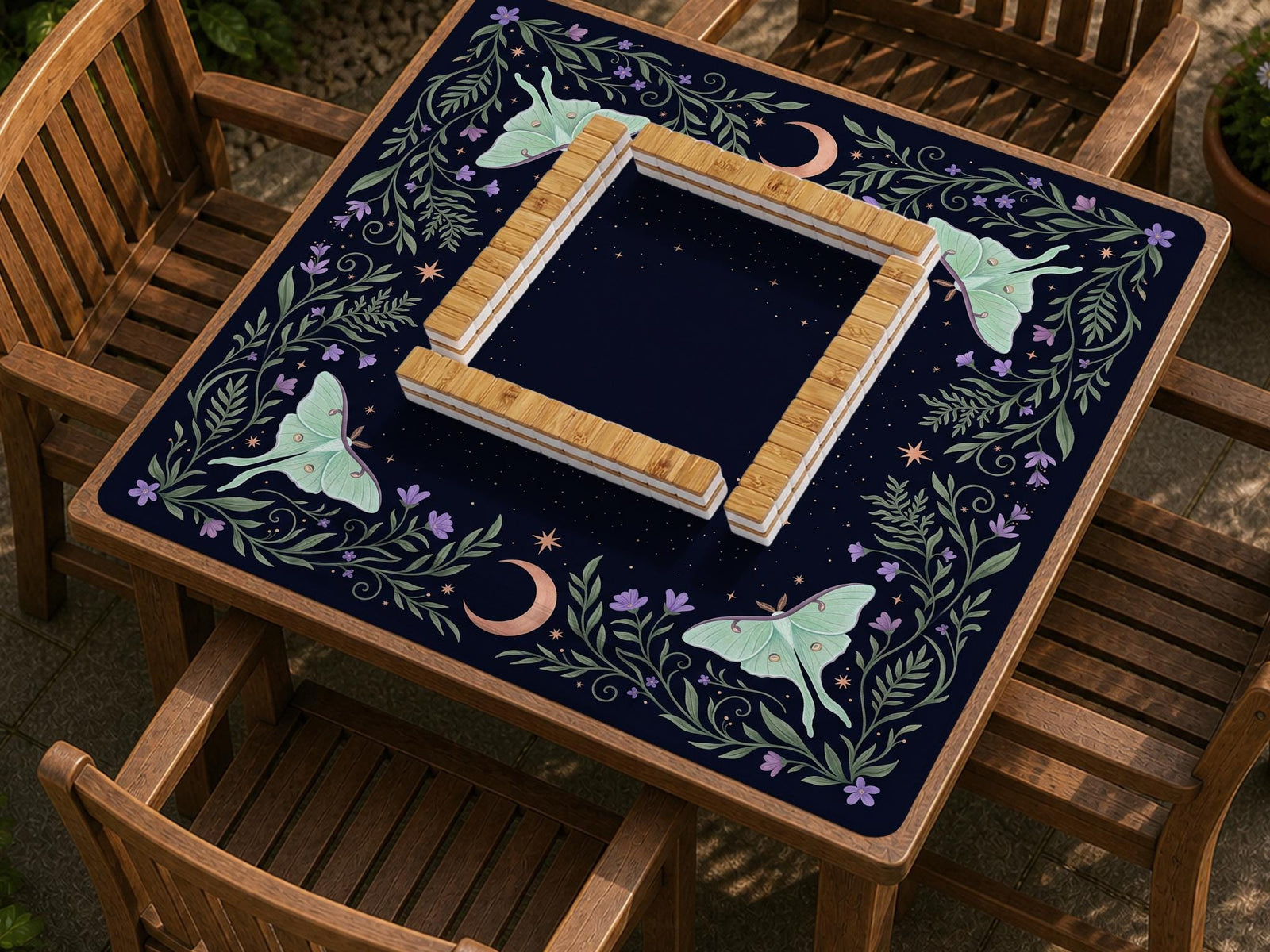 Navy square mahjong mat with a moon, moth, stars, and floral botanical border around an open center play area.