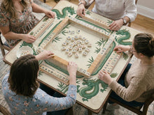 Ivory square mahjong mat with green dragon illustrations, bamboo stalks, clouds, a lotus center, and printed rules around the border.