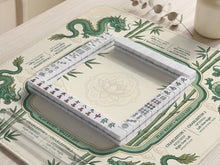 Cream mahjong mat with a green dragon design, bamboo details, and rule prompts along the border.