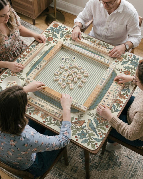 A floral mahjong mat with a cream background, botanical border, soft blue frame, vintage bird garden artwork, and printed rules.