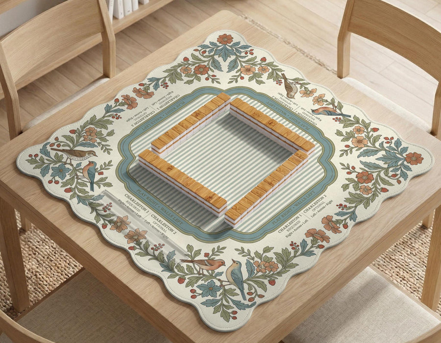 Scalloped square mahjong mat with bird illustrations, cream flowers, sage leaves, and a striped center with printed rules text.