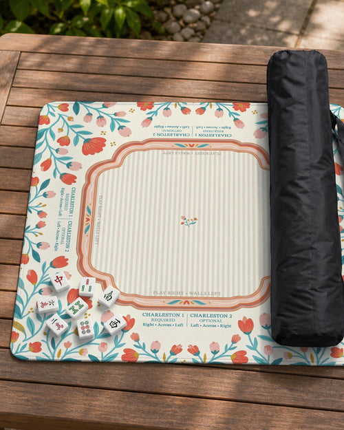 Square mahjong mat with a cream background, coral and teal folk floral border, and printed rules and tile layout details in the center.